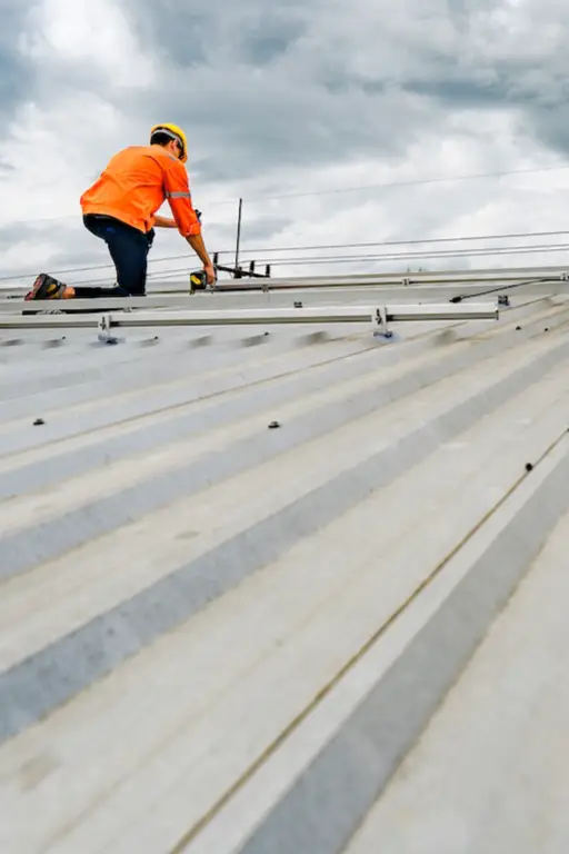 ouvrier refait etancheite toit metallique Ouvrier sur un toit métallique par temps nuageux.